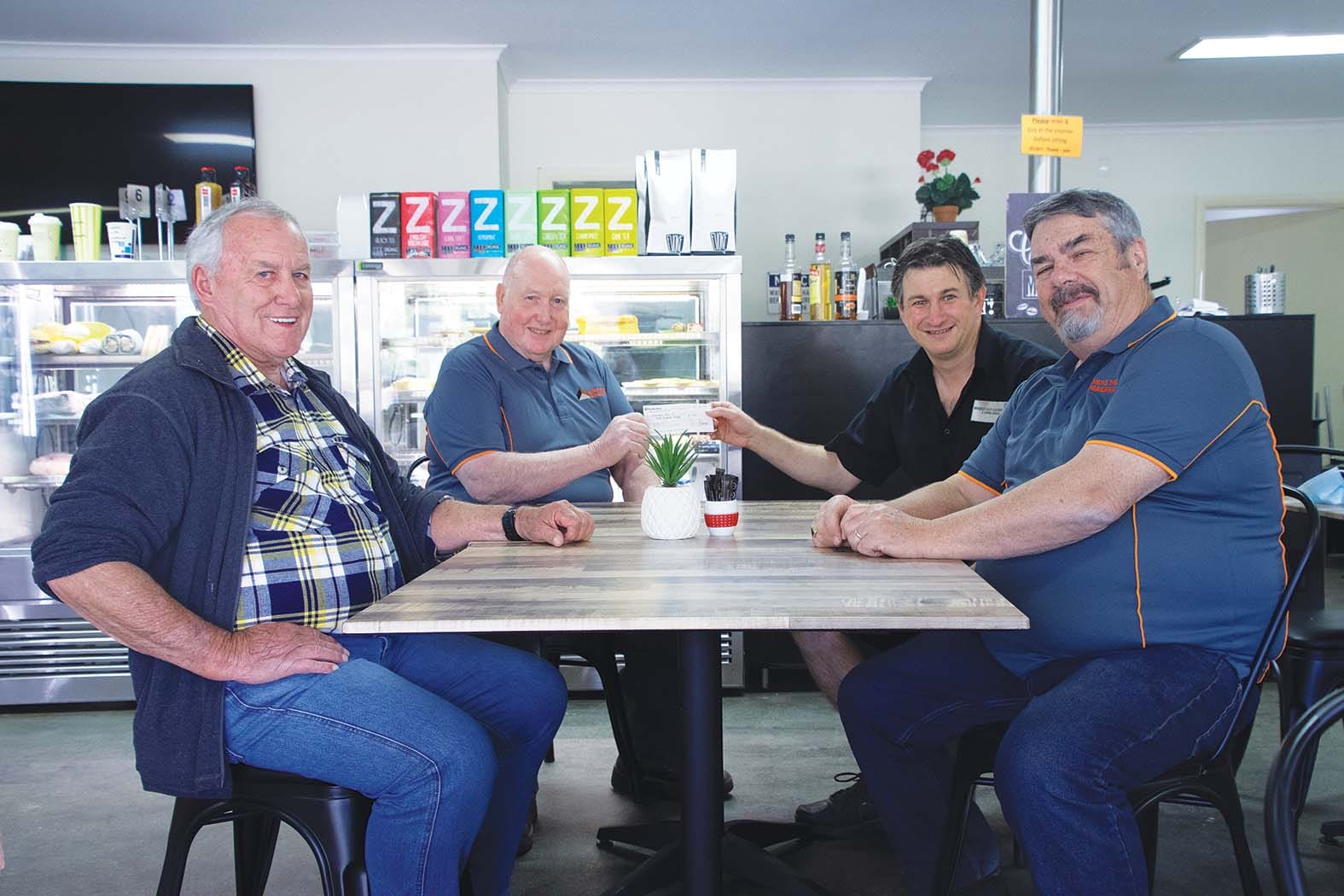 Win-win situation... (From left): Men’s Shedders Dennis Baydon, Norm McLaughlan and Alan Anderson try out the chairs and tables they put together while they accept a cheque for $300 from David Brereton (second right). 